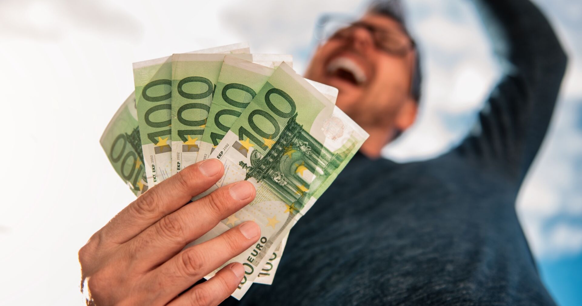 Porträt eines jubelnden Mannes mit Geldscheinen in einer Hand