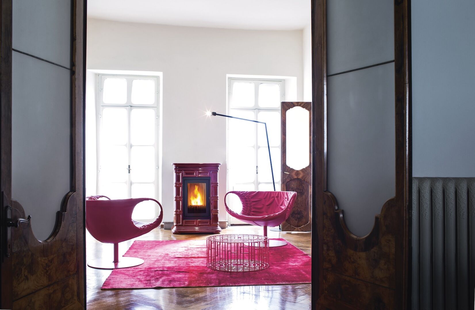 Blick in Wohnzimmer mit pinkem Teppich, pinken Sesseln und pinkem Pelletsofen