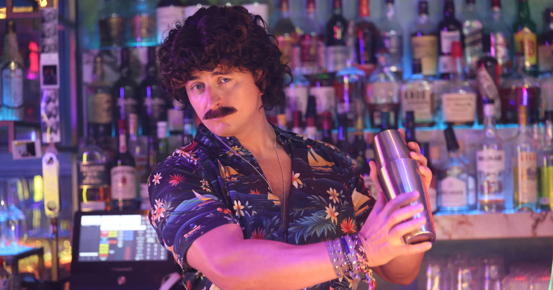 Mann mit Schnauzer steht hinter Bar und mixt Cocktails