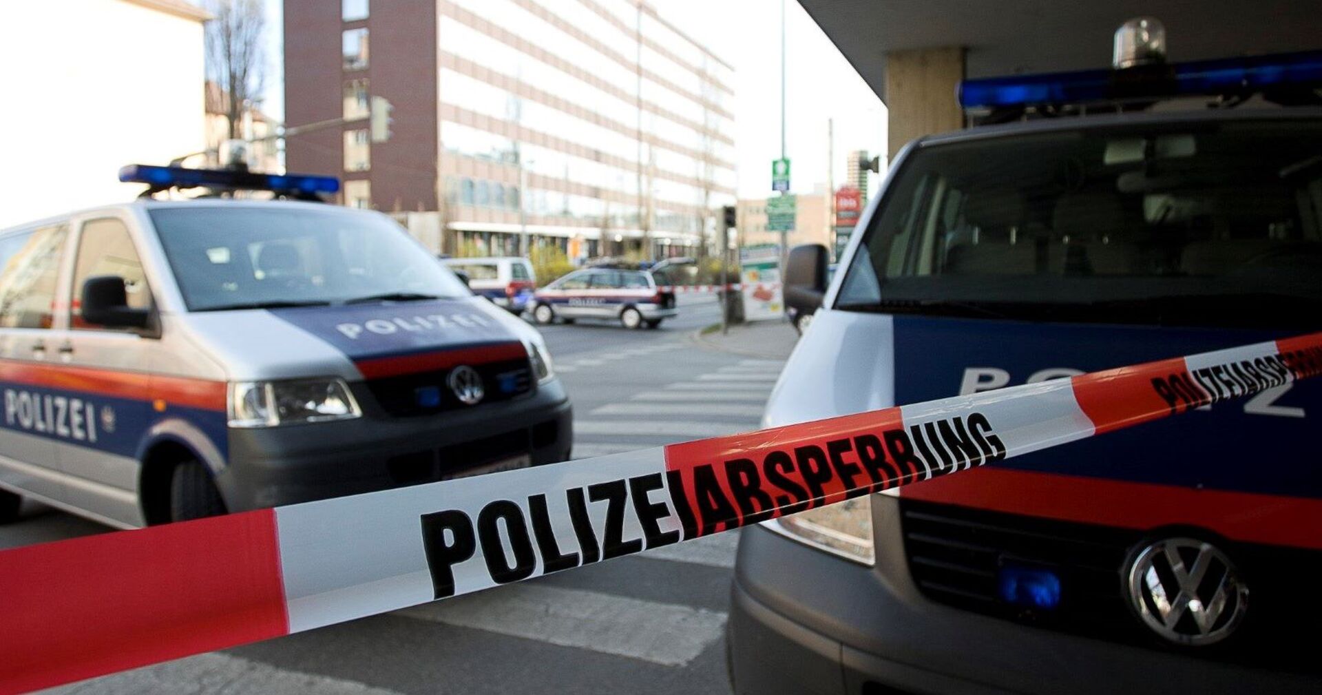 Polizeiabsperrung und zwei Einsatzfahrzeuge vor einem Gebäude.