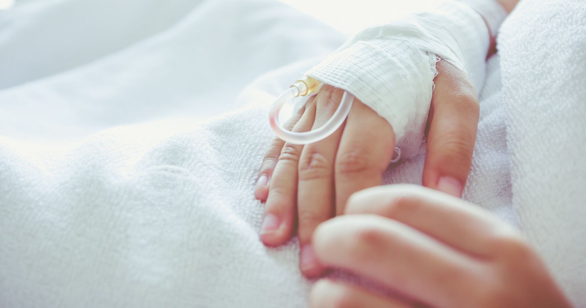 Ein kleiner Bub liegt im Spital, jemand hält seine Hand.