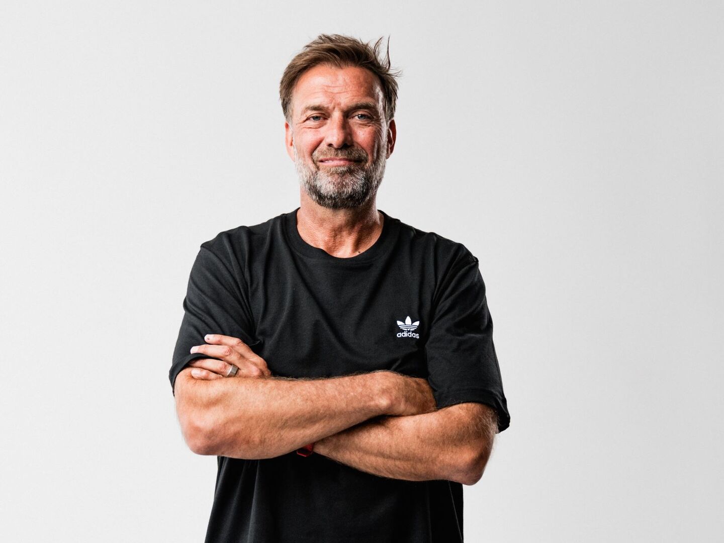 Jürgen Klopp mit Grinsen, verschränkten Armen und im schwarzen T-Shirt.