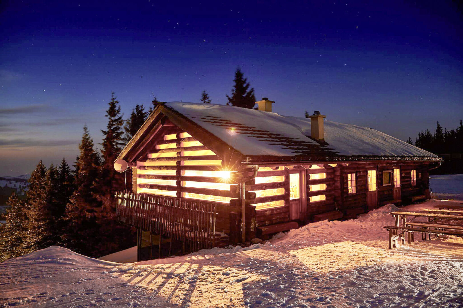 Eine beleuchtete Almhütte umgeben von Schnee
