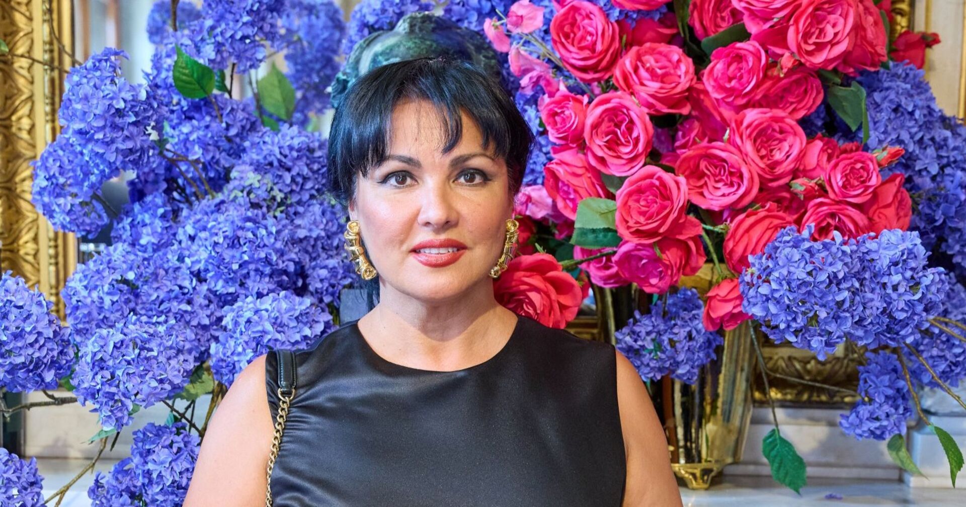 Anna Netrebko vor einer Blumenwand.