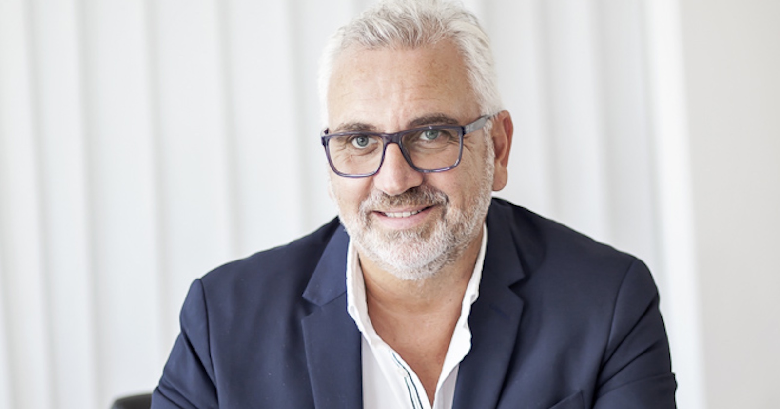 Mann mit weißem Haar und dunkelblauen Sakko