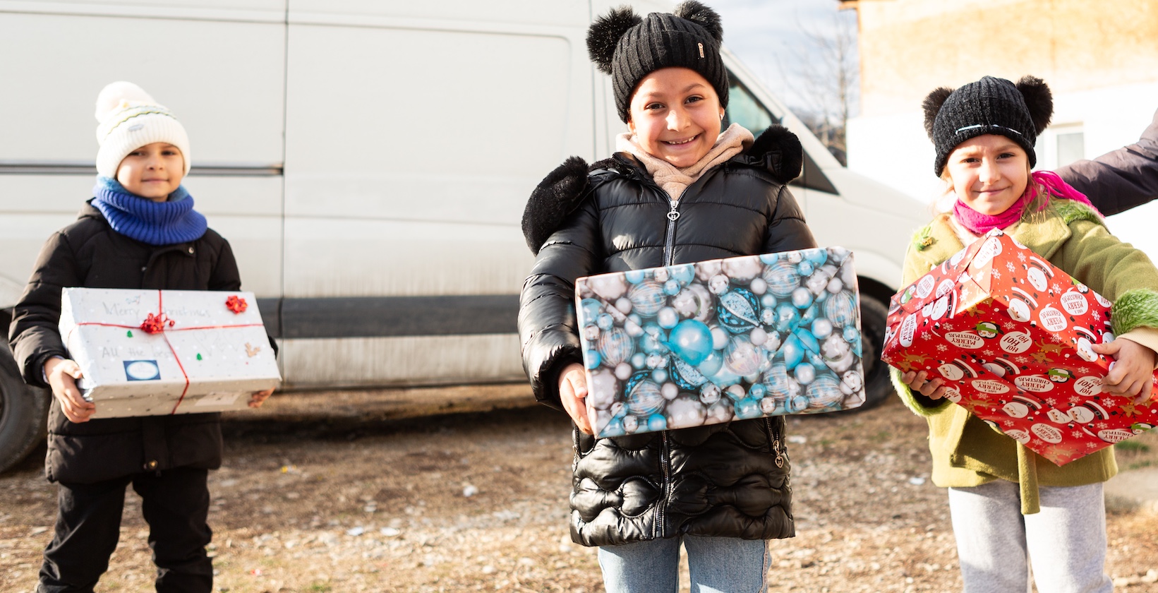 drei Kinder mit Geschenken vor einem weißen Bus