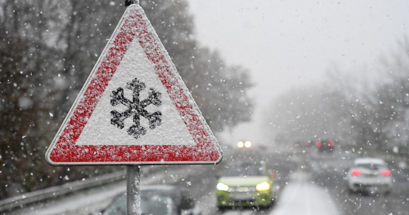Winterliche Verhältnisse auf einer Straße und ein Schneefall-Warnschild.