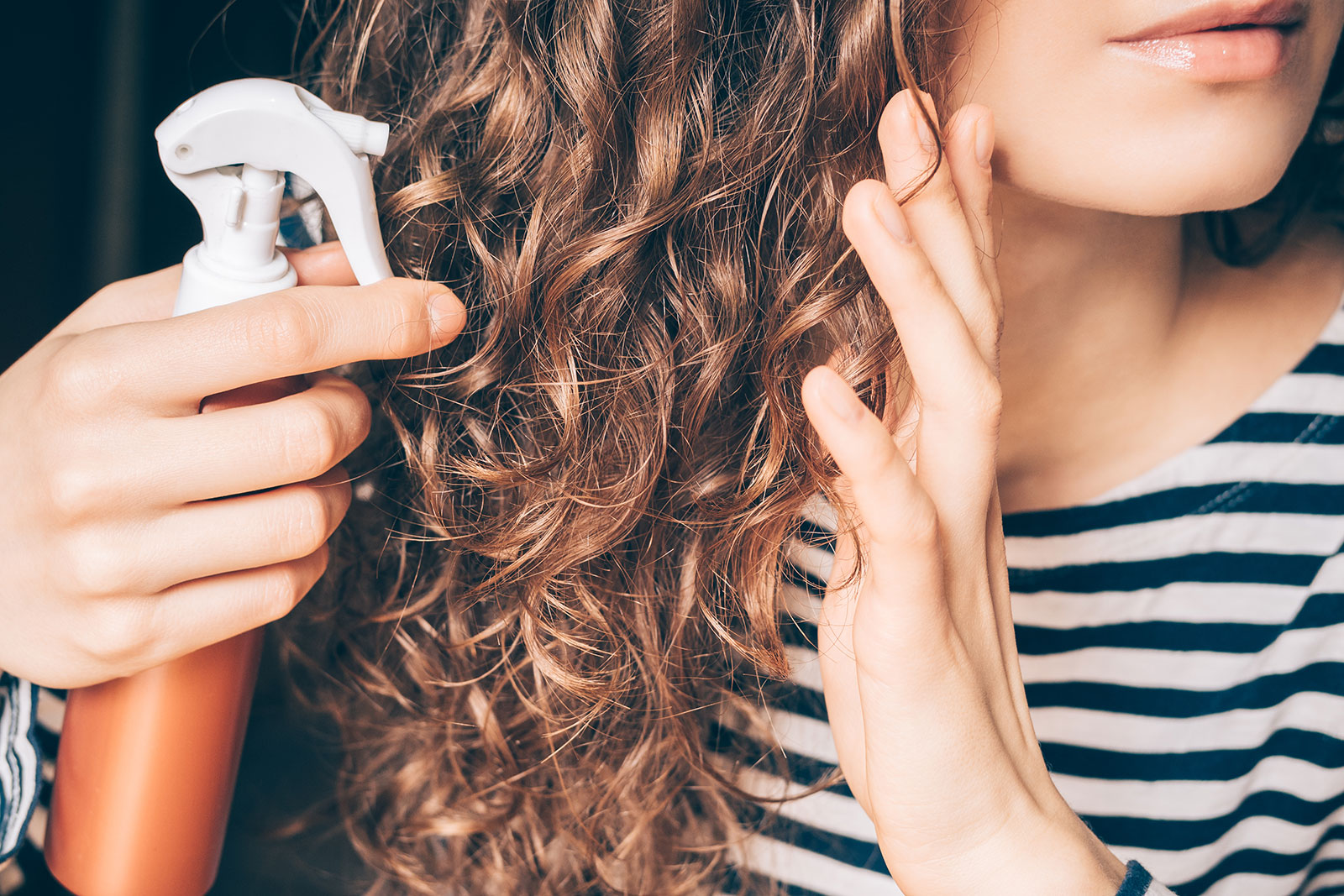 Frau sprüht ihre gelockten Haare mit einem Pflegespray ein | Credit: iStock.com/iprogressman