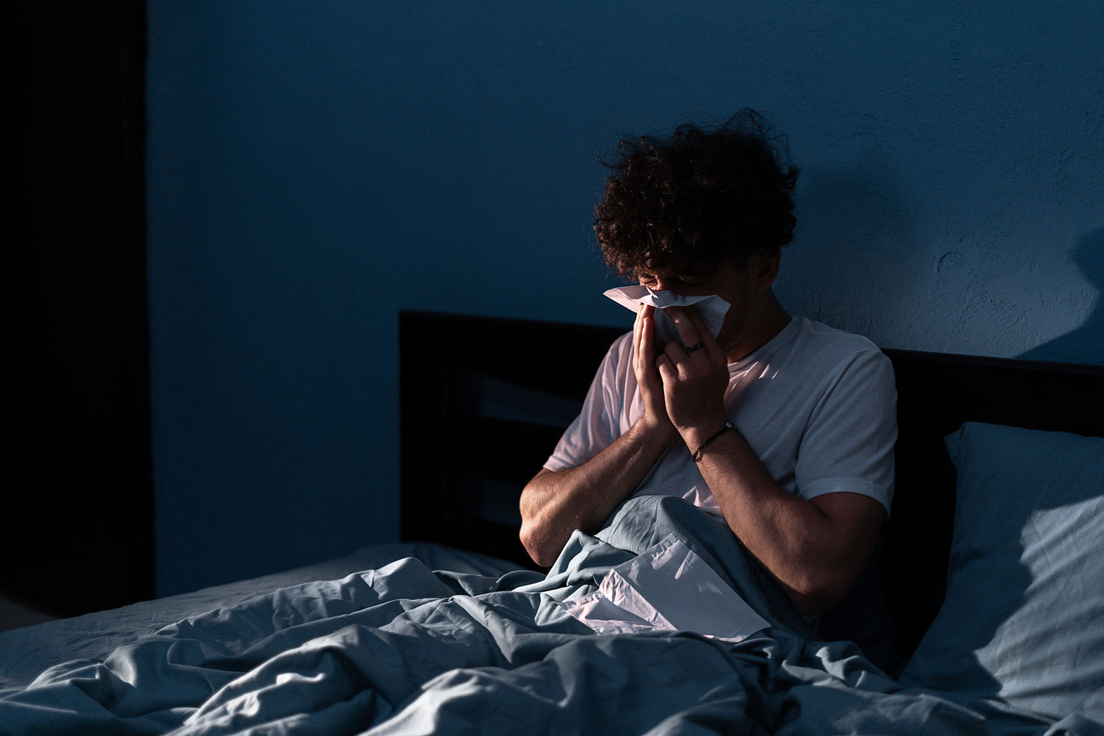 Mann niest im Bett | Credit: iStock.com/Andrii Lysenko