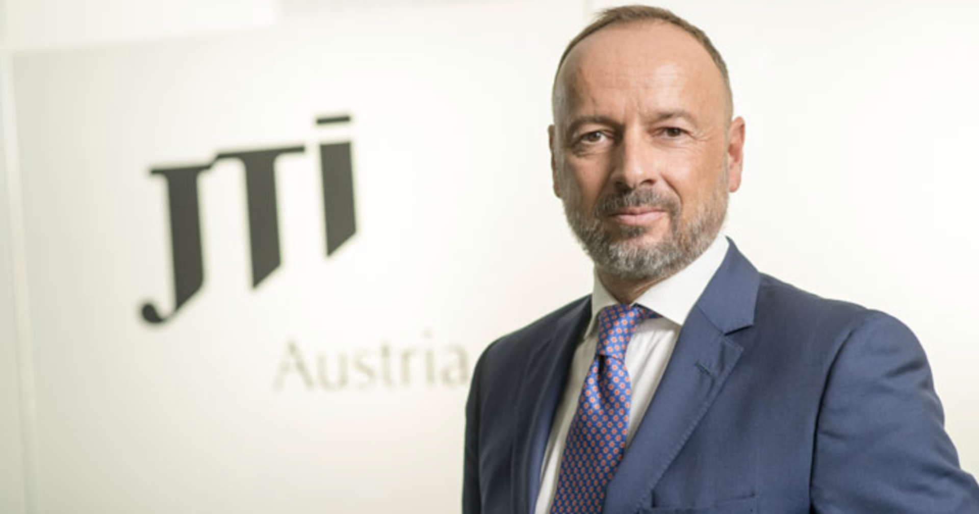 JTI-Kommunikationsexperte im Anzug vor einem Firmenplakat