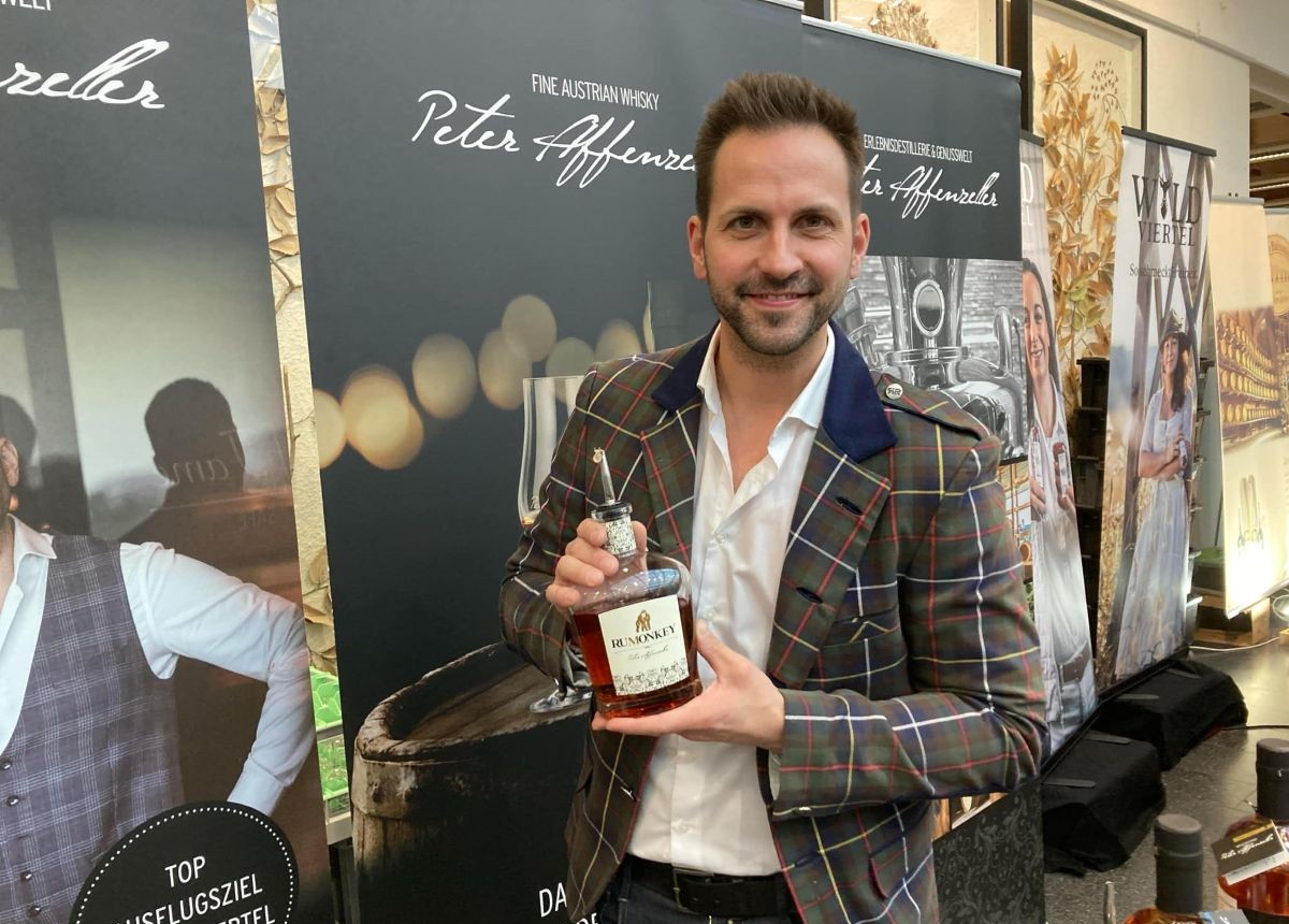 Peter Affenzeller - etwas unrasiert - und mit einem Sakko, das vom Muster an einen Kilt erinnert, lacht. Er hält in beiden Händen seinen Rumonkey.