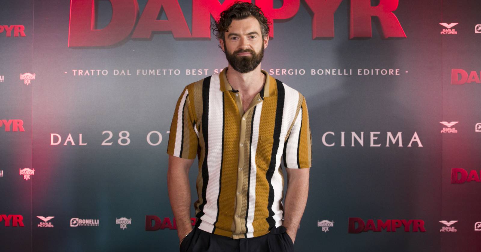 Der Schauspieler Stuart Martin, der ein schwarz-weiß-braun kariertes Hemd trägt und für die Fotografen auf einem Roten Teppich posiert