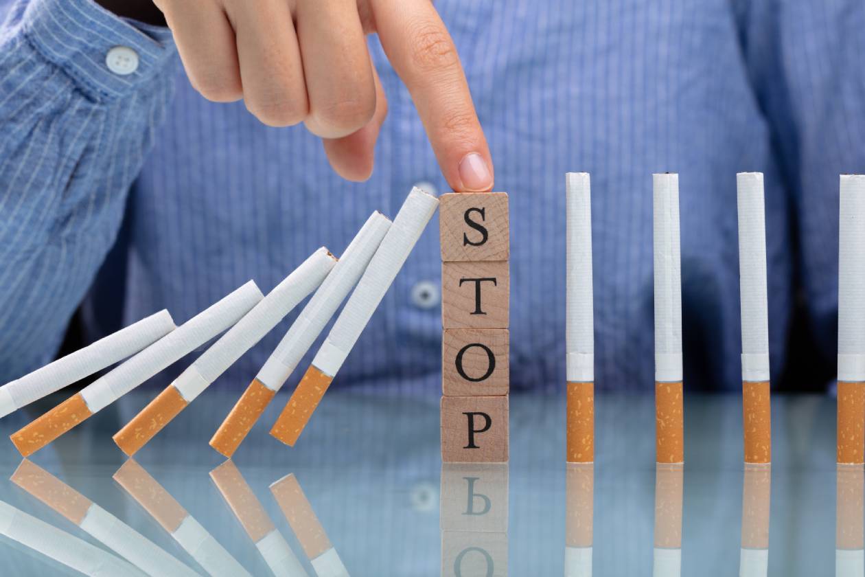 Eine Reihe umfallender Zigaretten, die von vier aufeinander gestapelten Bausteinen, auf denen das Wort "Stop" zu lesen ist, aufgehalten werden