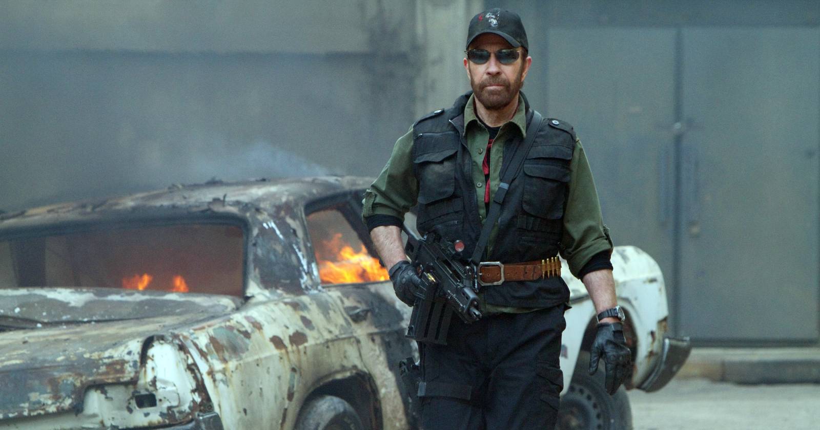 Eine Szene aus "The Expandables 2", in der Chuck Norris mit einer Maschinenpistole in der Hand neben einem brennenden Auto steht