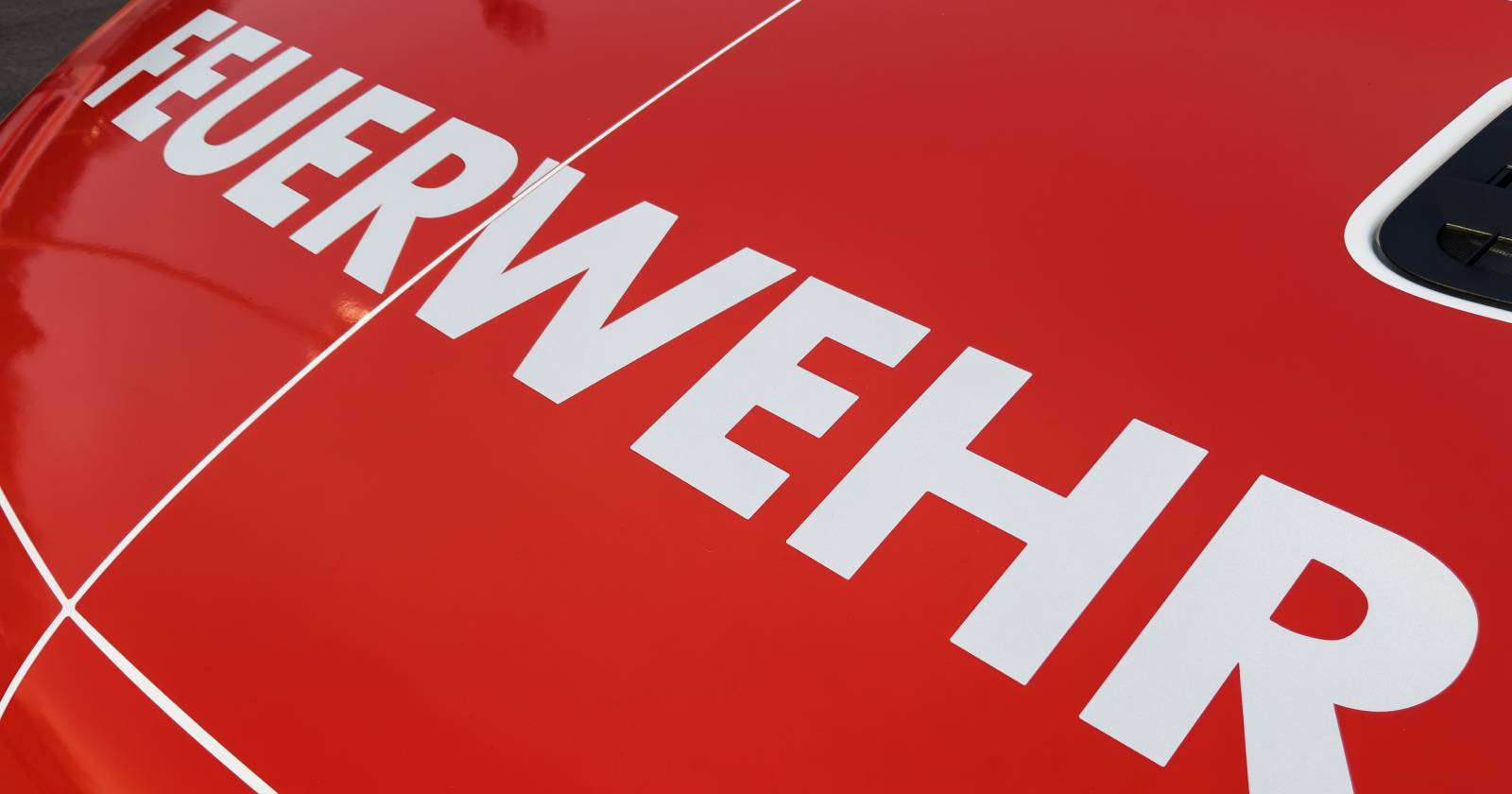 Nahaufnahme der Motorhaube eines Feuerwehrfahrzeuges, auf der der weiße Schriftzug "Feuerwehr" zu lesen ist