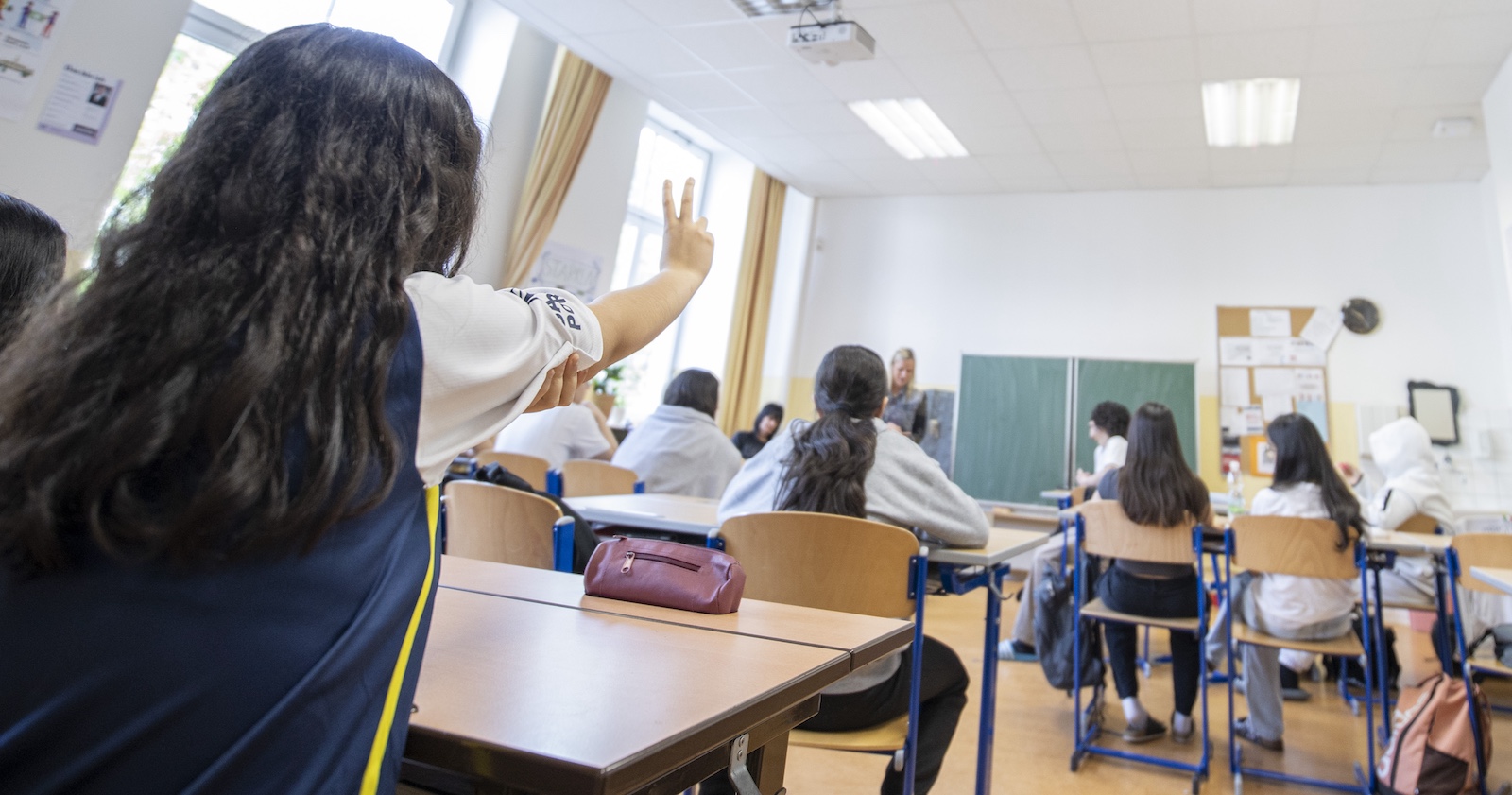 Szene aus einem österreichischen Klassenzimmer, ein Mädchen zeigt auf