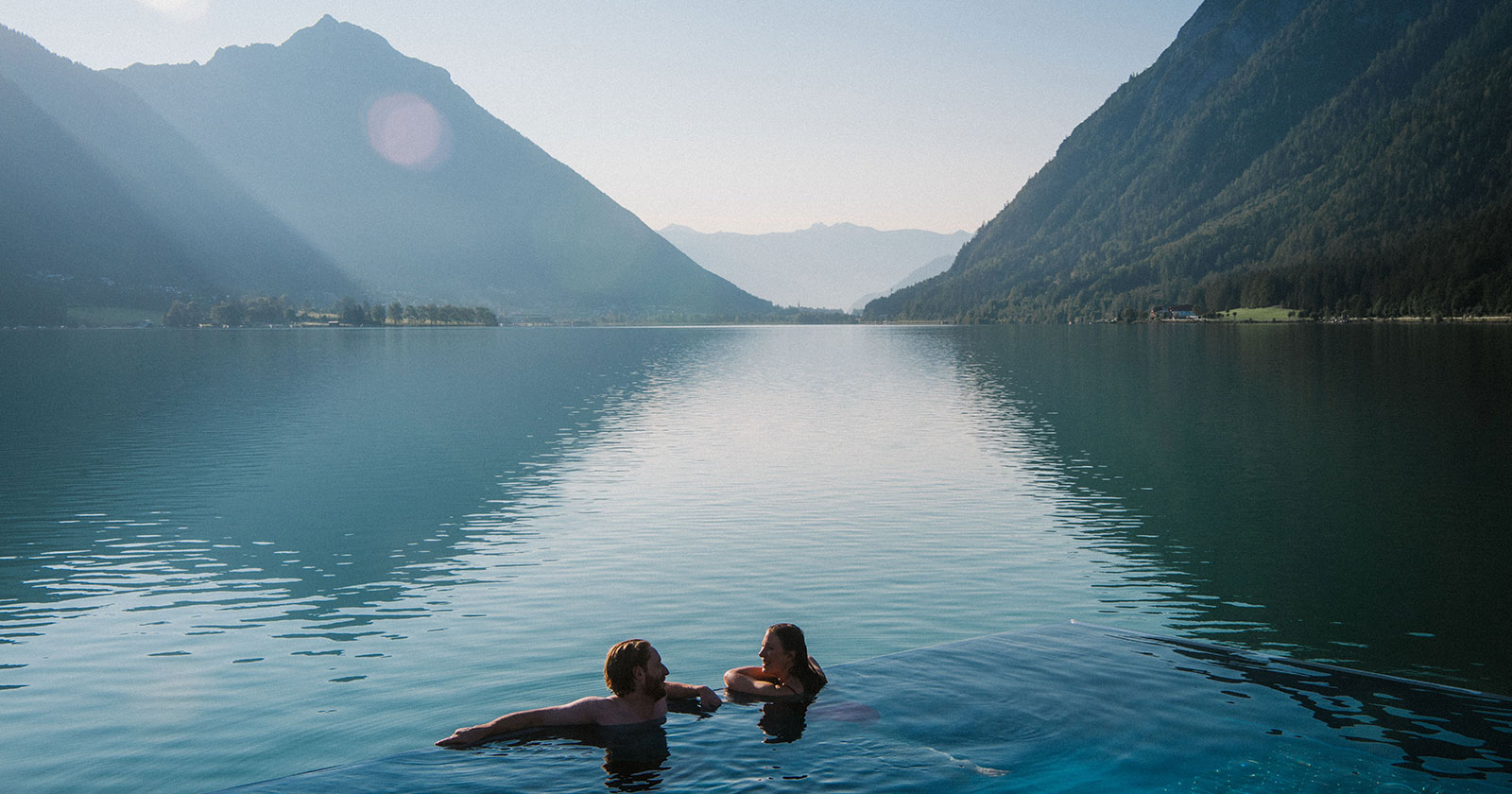 Pärchen beim Schwimmen in einem See bei Sonnenaufgang | Credit: Tirol Werbung/Dominic Zimmermann