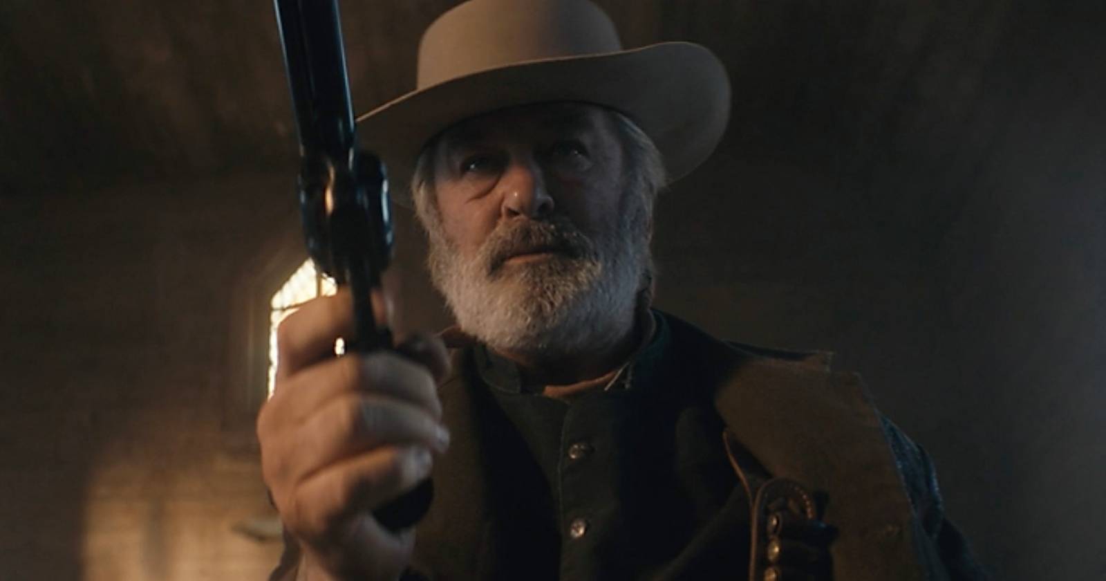 Szene aus dem Western "Rust", die Alec Baldwin zeigt, der einen Cowboy-Hut trägt und mit einem Revolver auf die Kamera zielt