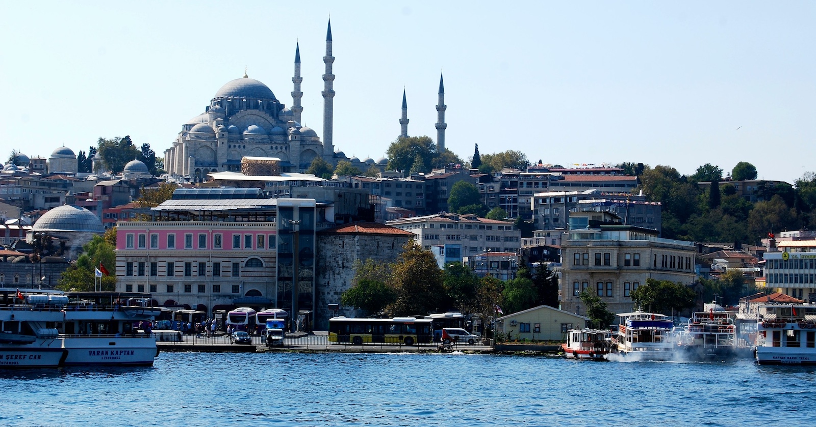 Panorama von Istanbul mit der Süleymaniye-Moschee im Hintergrund, davor der Bosporus mit mehreren Booten und Fähren bei sonnigem Wetter.
