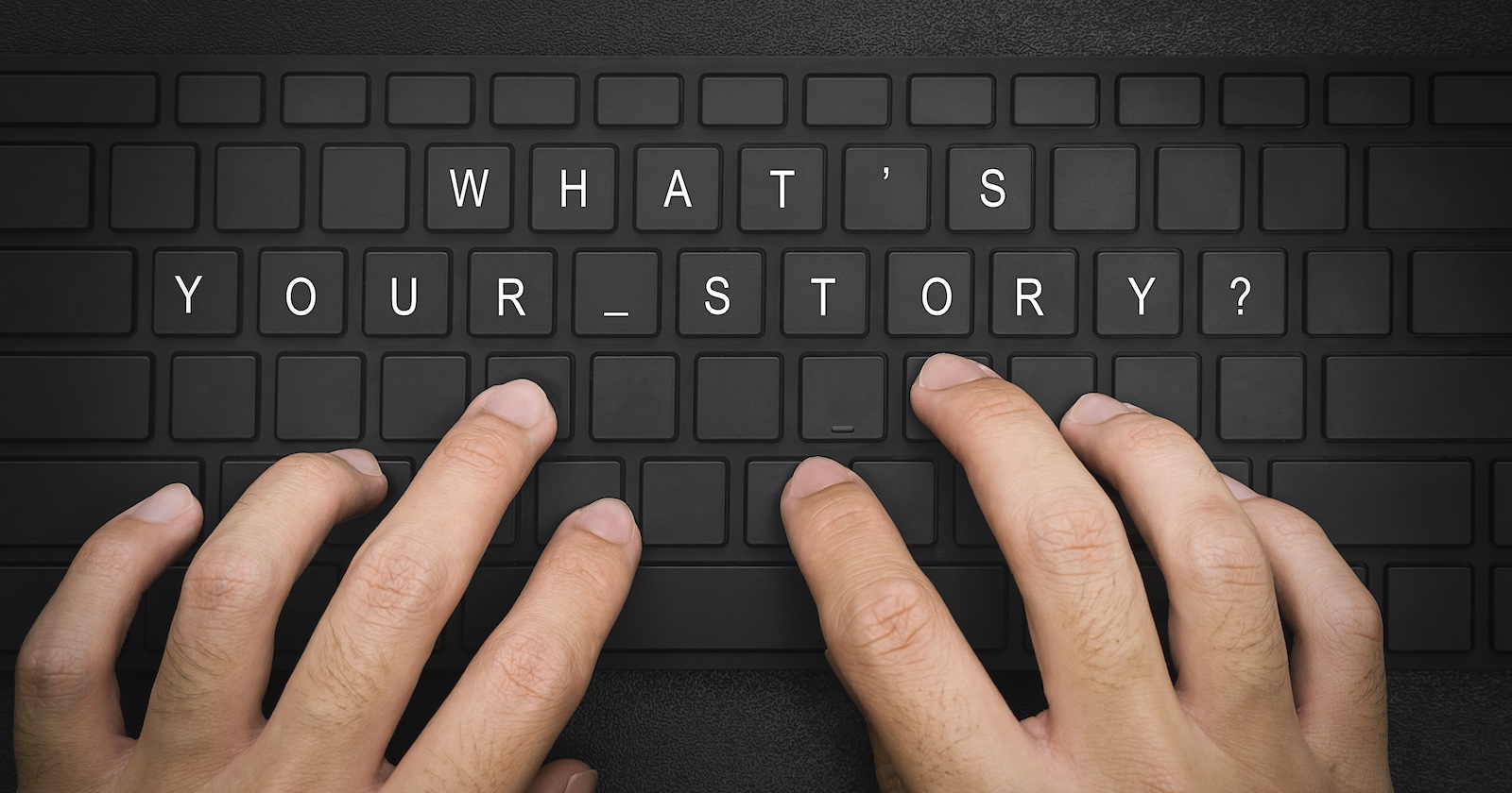 Zwei Hände tippen auf einer Tastatur, wo "What's your Story?" draufsteht.