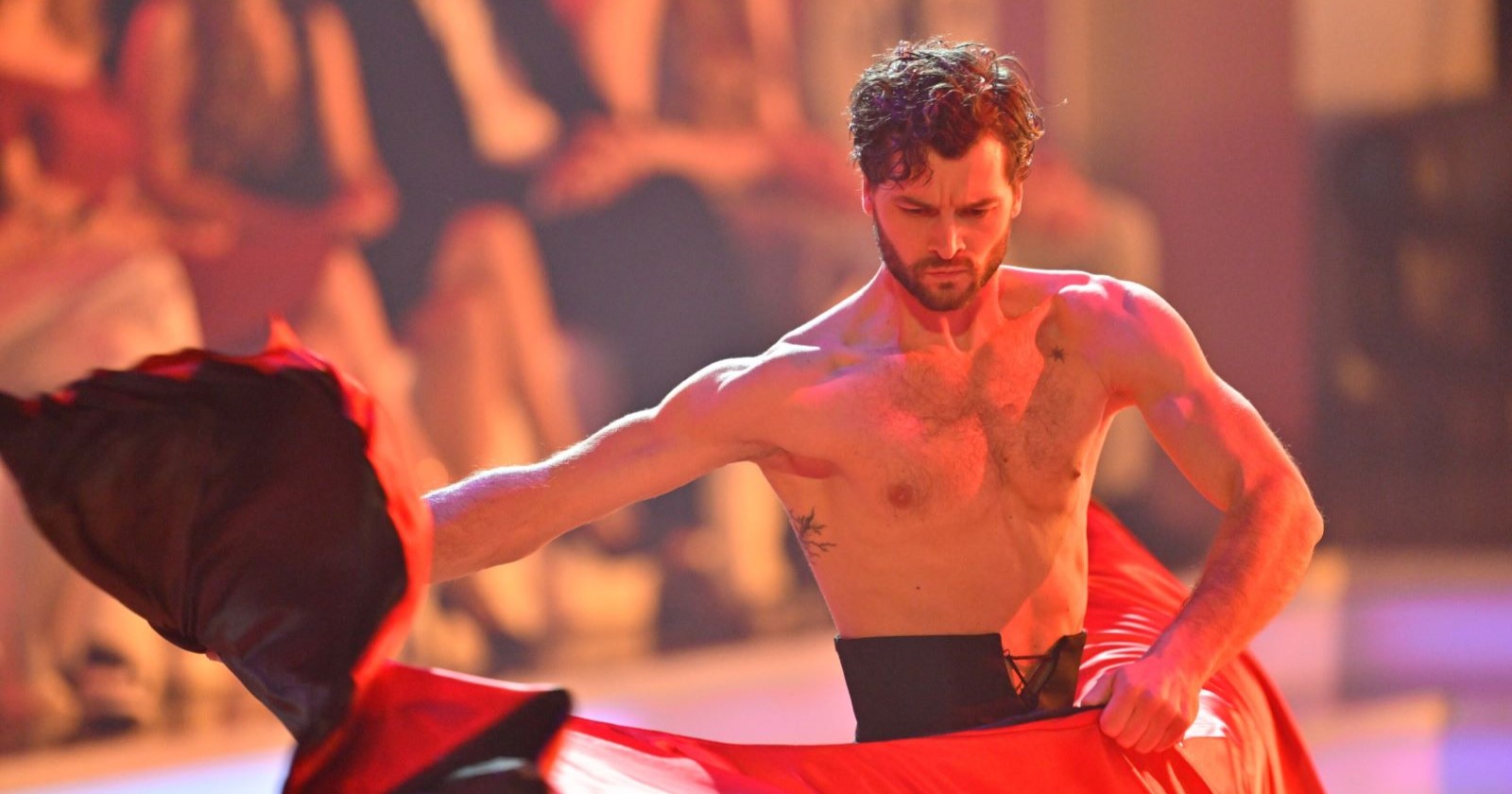 Aaron Karl tanzt im Finale von Dancing Stars 2025 einen Paso Doble ohne Hemd. Mit ernstem Blick und rotem Tuch führt er eine kraftvolle Pose aus, Zuschauer im Hintergrund.