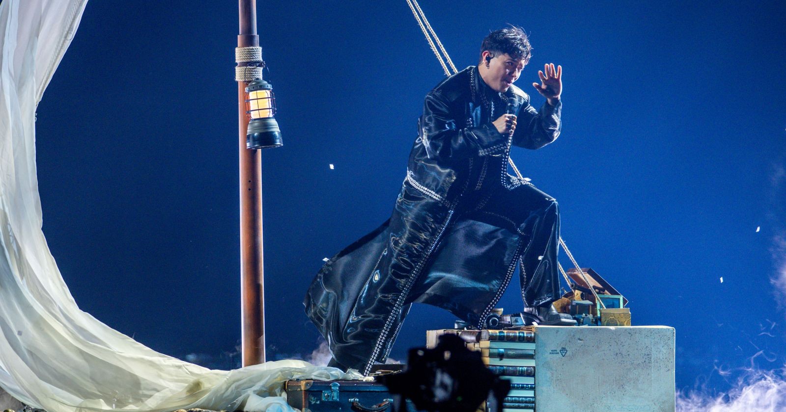 JJ beim ESC 2025-Halbfinale auf einer symbolischen Segelboot-Bühne in Schwarz-Weiß-Optik, gekleidet in langen Mantel und umgeben von Nebel.