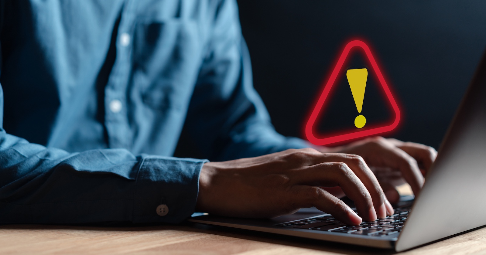 Ein Mann sitzt vor einem Laptop und ein Rufzeichen.