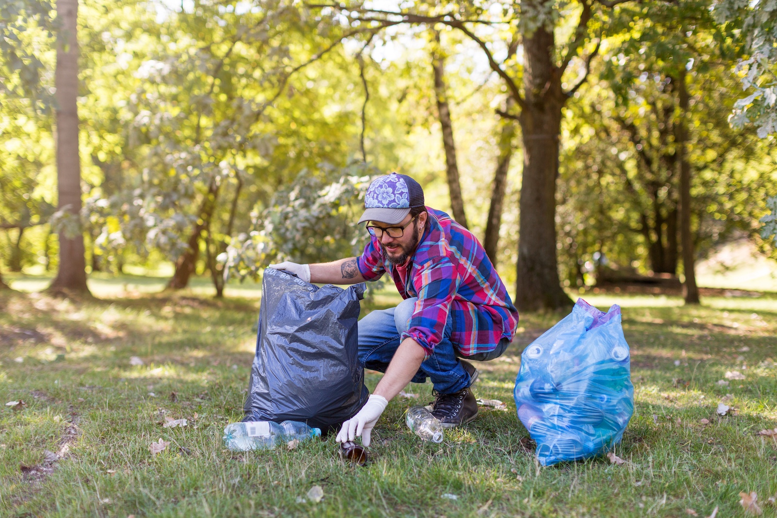 Ein Mann mit Kappe sammelt auf einer Wiese Müll ein.