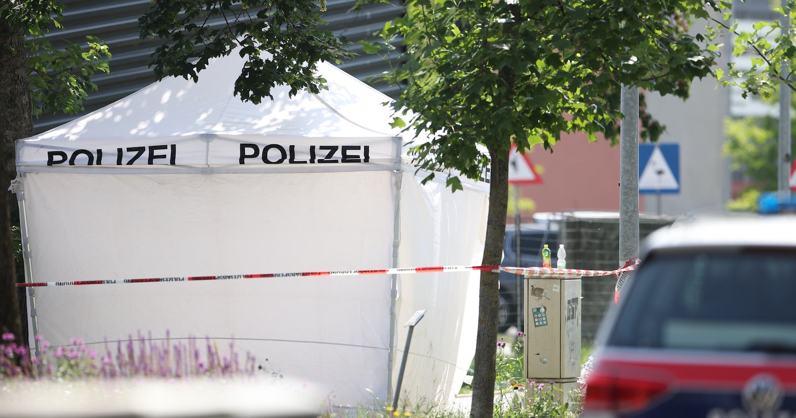 Weißes Polizei-Zelt hinter Absperrband an einem von Bäumen gesäumten Tatort in Graz nach dem Amoklauf an einer Schule.
