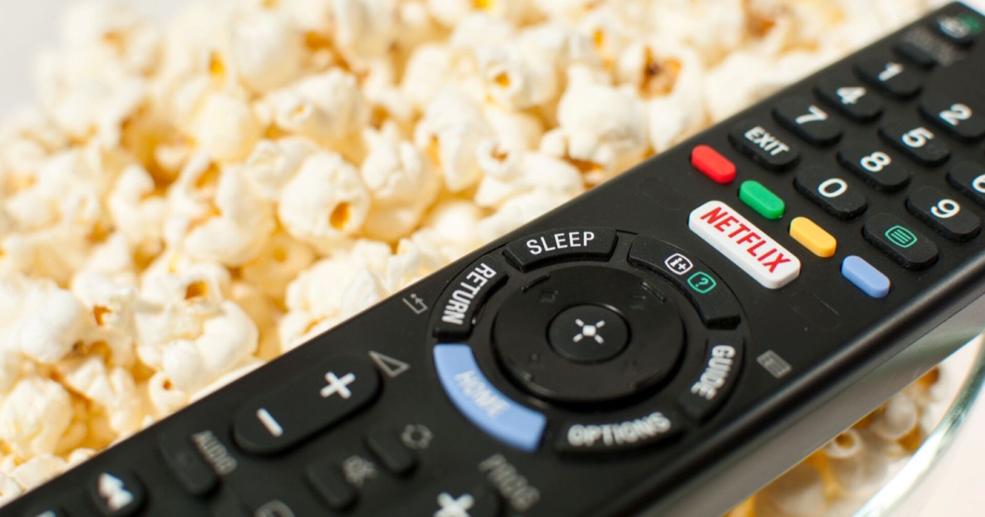 schwarze Fernbedienung mit weißem Netflix-Knopf mit roter Aufschrift "Netflix", liegt auf Popcorn