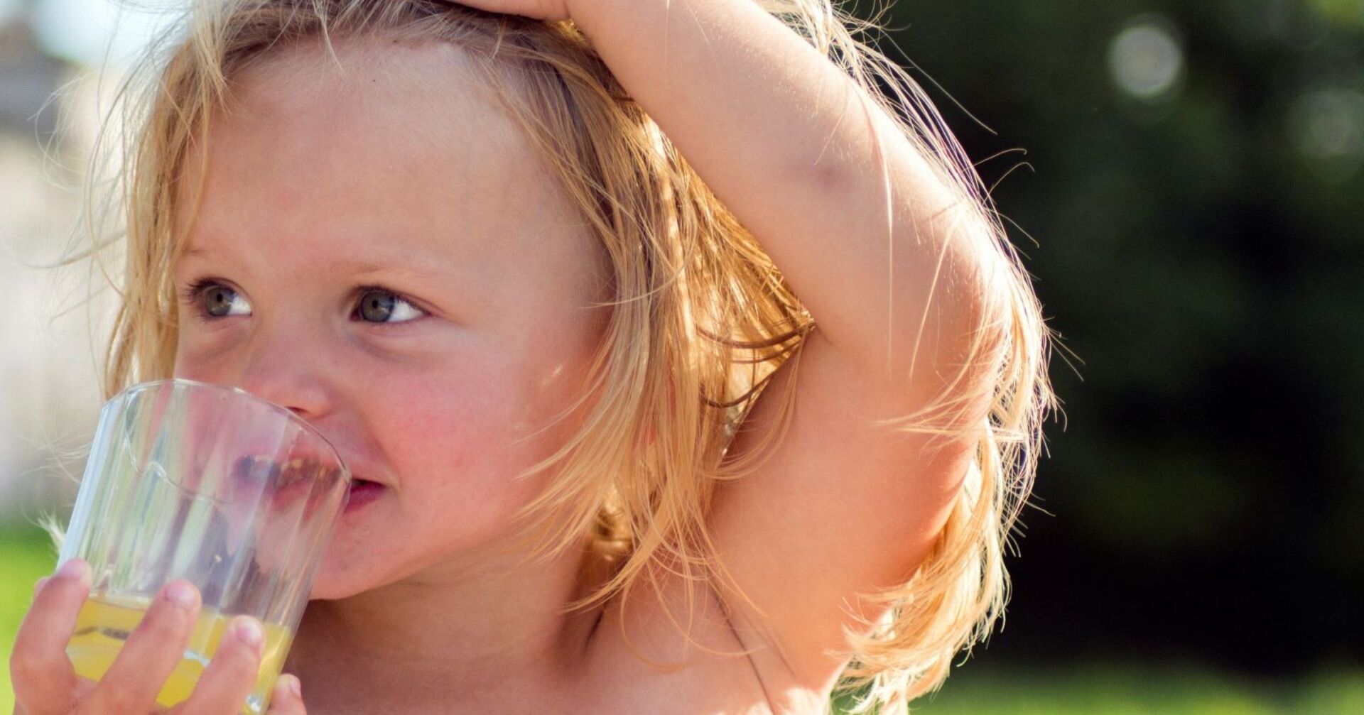 Mädchen trinkt Saft im Sommer, hält Hand an Kopf, Schutz vor Überhitzung und Hitzeschock bei Hitze.