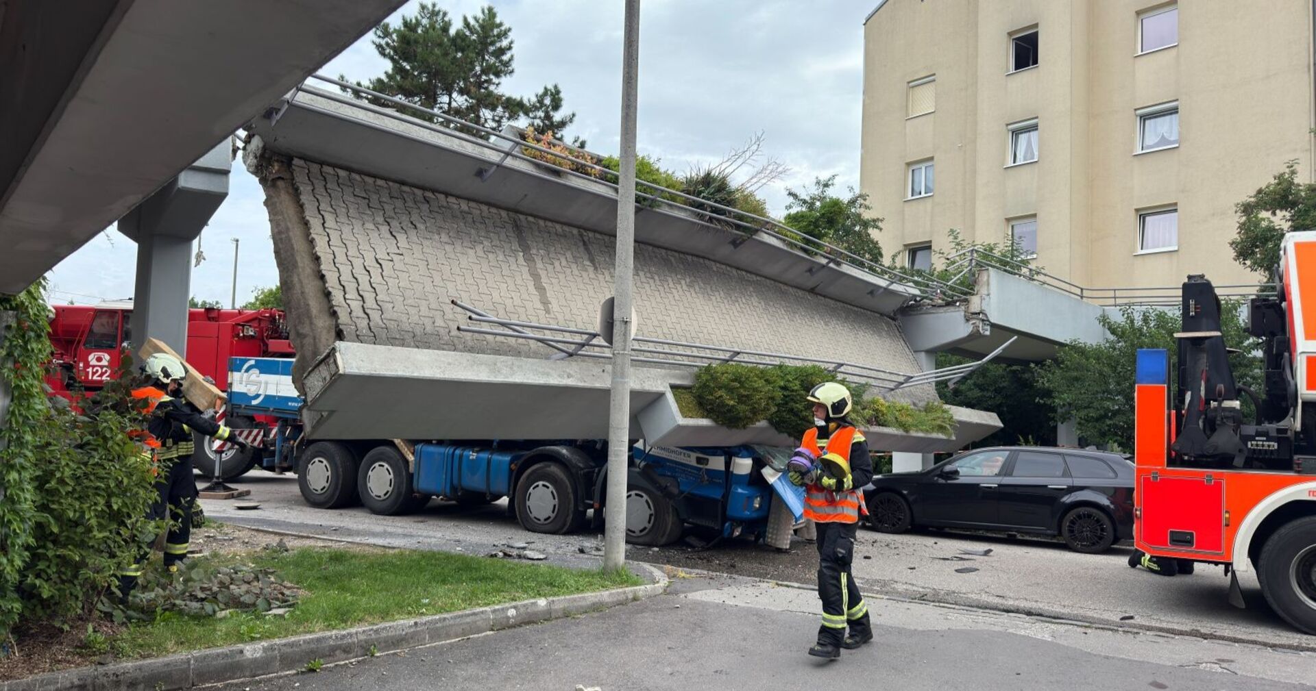 Feuerwehrleute arbeiten an einer eingestürzten Fußgängerbrücke in Linz, die auf einen Lastwagen gefallen ist. Der Lkw ist unter der Betondecke eingeklemmt, rundherum stehen Einsatzfahrzeuge.