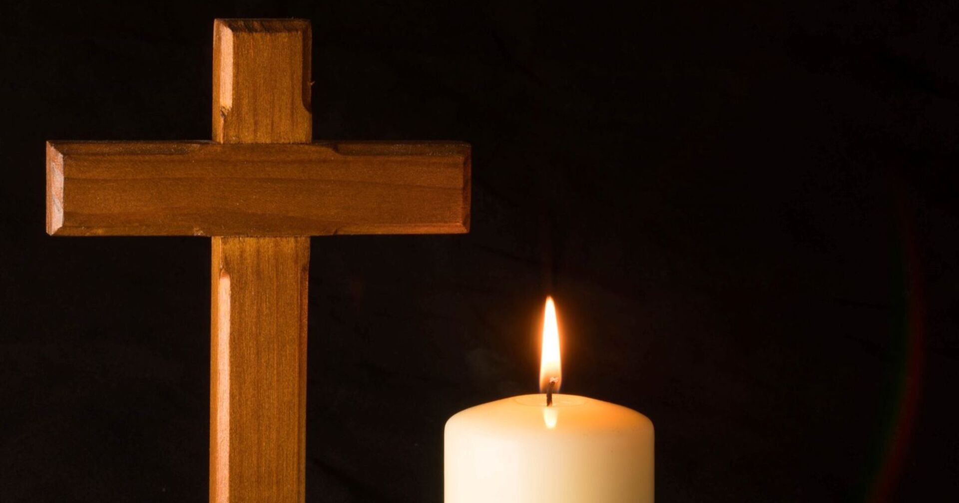 Eine leuchtende weiße Kerze mit einem Holzkreuz vor schwarzem Hintergrund als Zeichen für Trauer