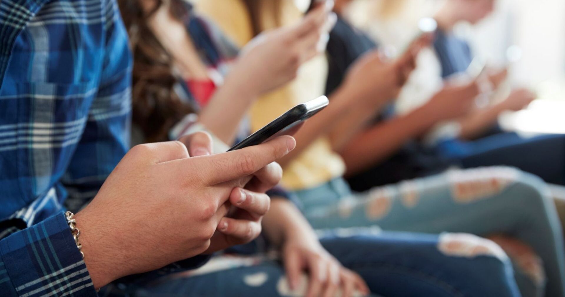 Jugendliche sitzend, mit Smartphone in der Hand