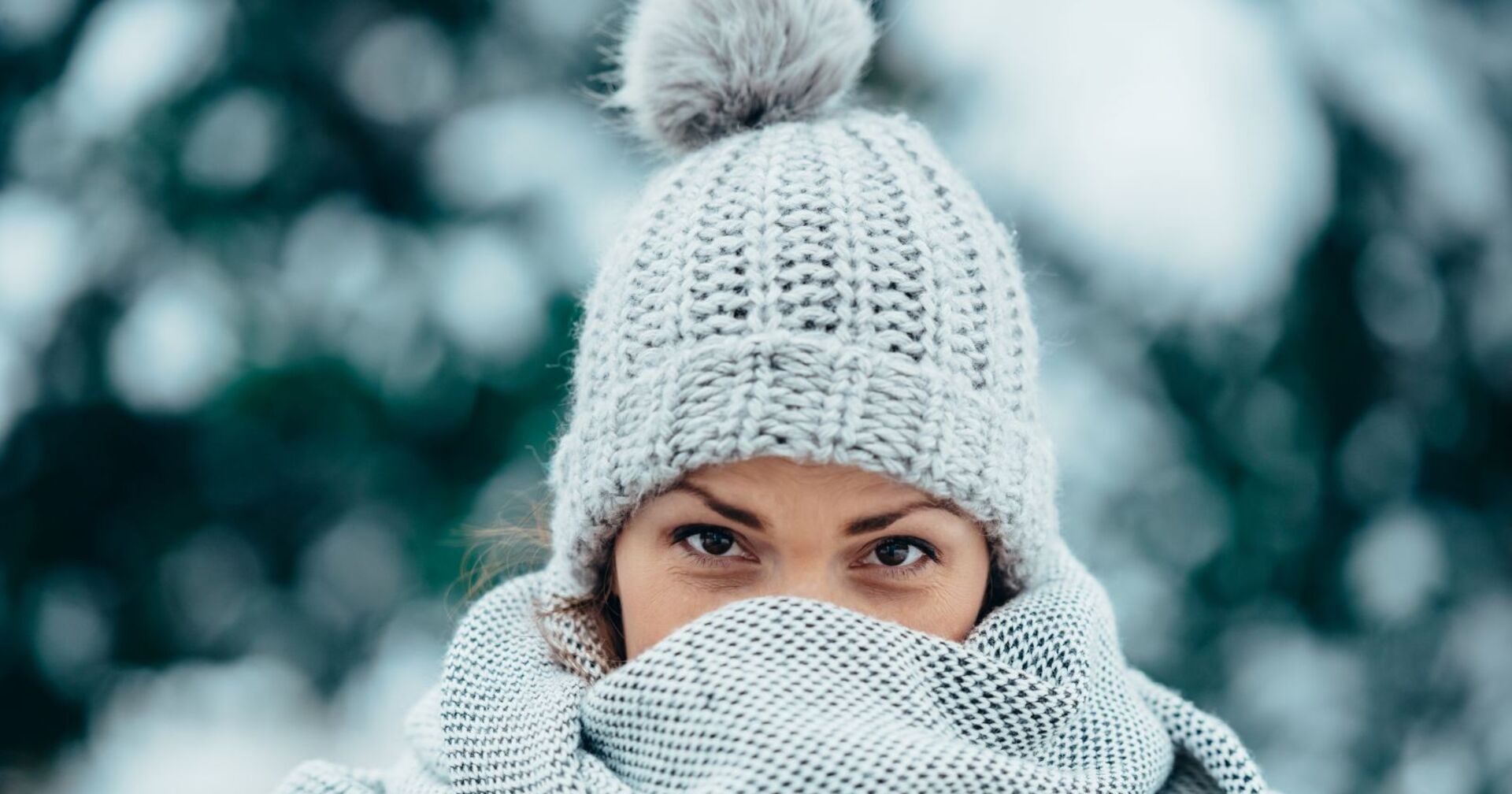 Junge Frau in Winterbekleidung steht vor verschneiten Bäumen