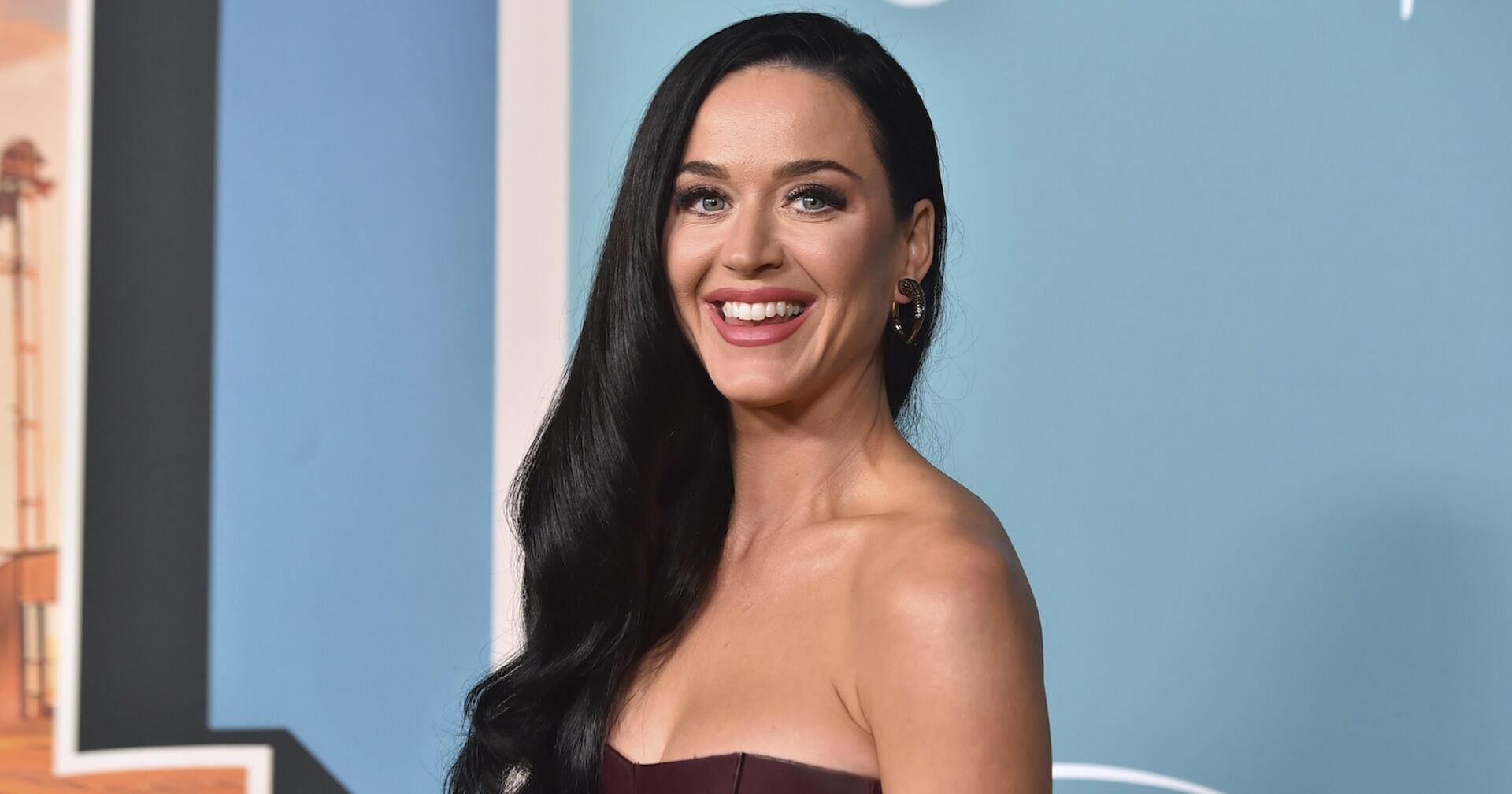 Katy Perry mit offenen, schwarzen Haaren vor blauem Hintergrund