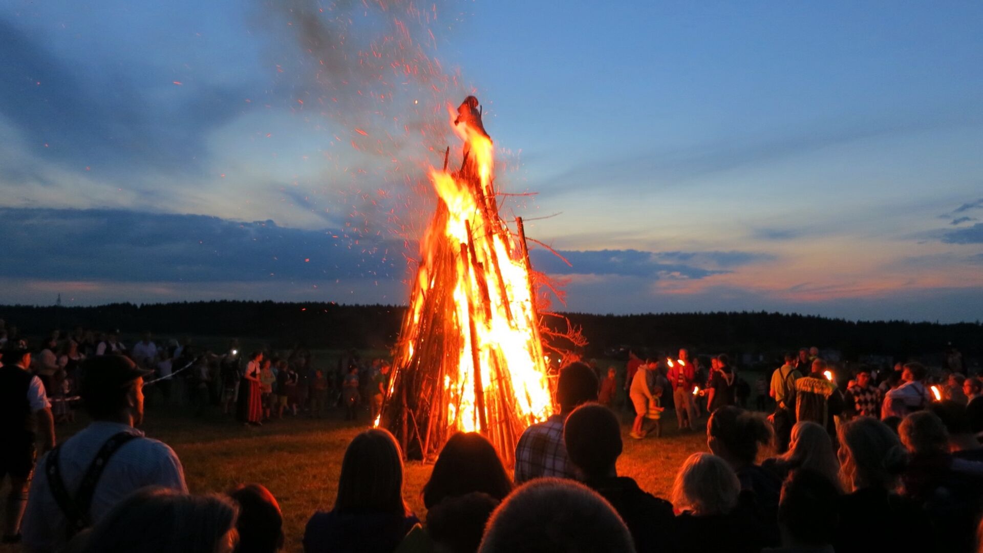 Viele Menschen stehen rund um ein Sonnwendfeuer.