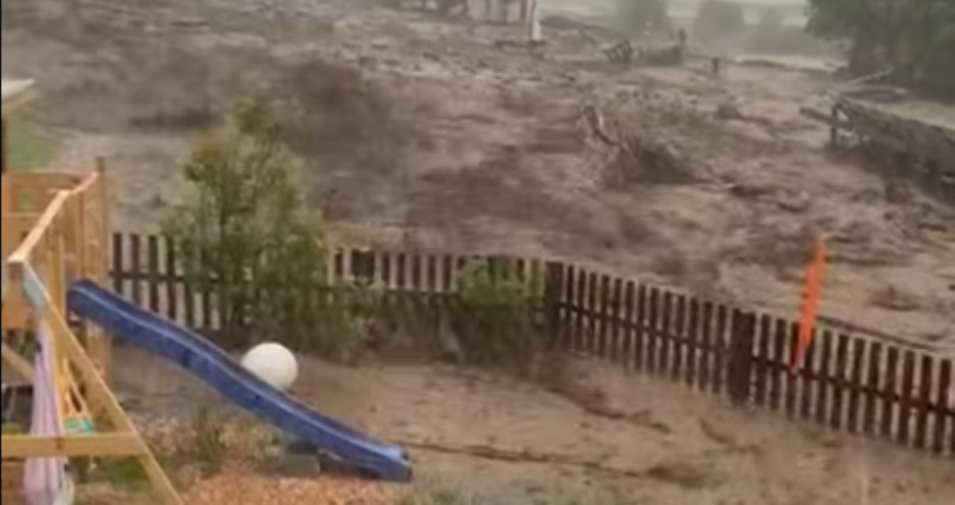 Schlammflut nach Murenabgang in Tirol: braune Wassermassen durchbrechen einen Holzzaun nahe eines Spielplatzes in Gschnitz.
