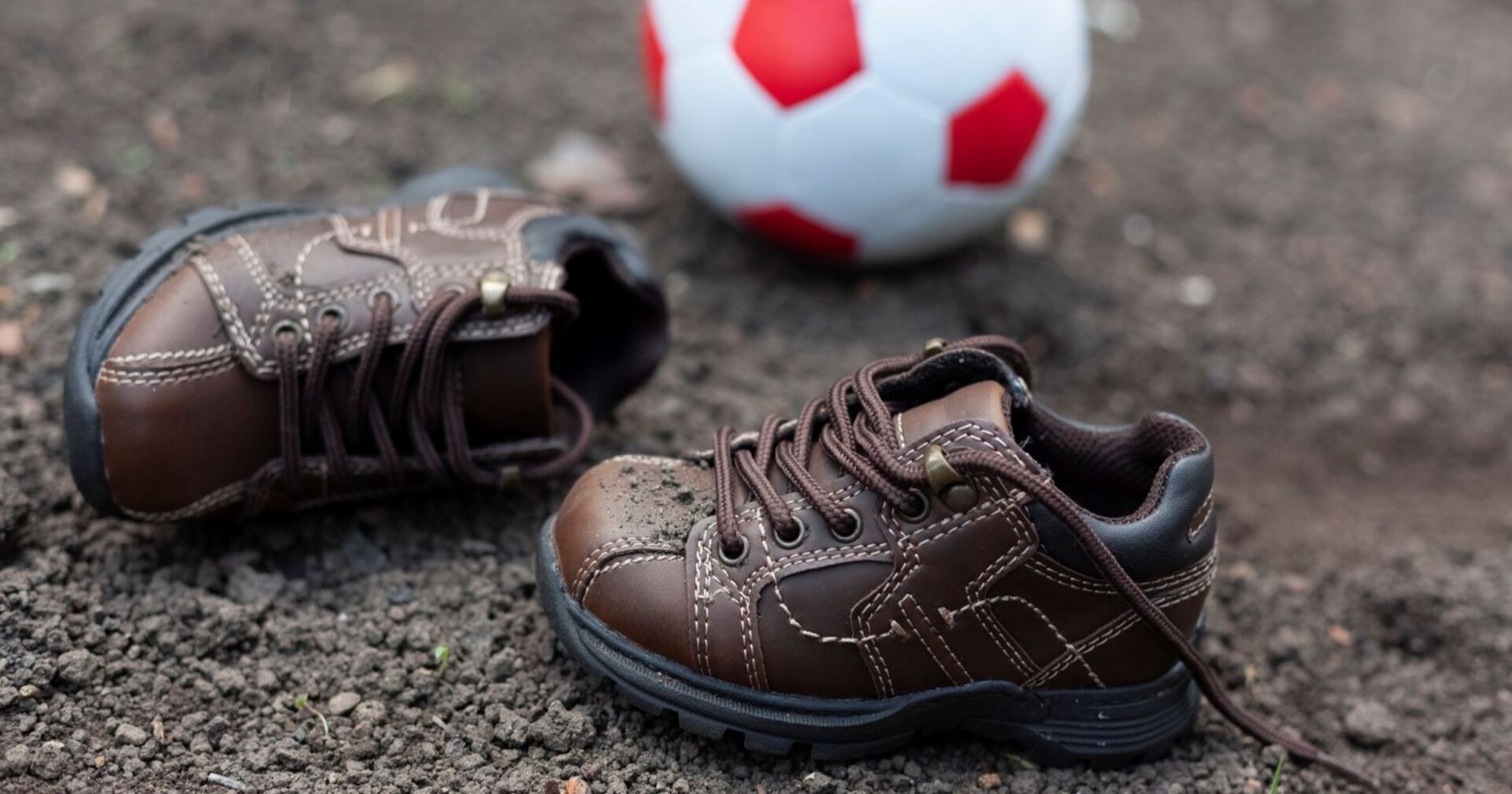 Kinderschuhe auf matschigem Boden, im Hintergrund liegt ein Fußball