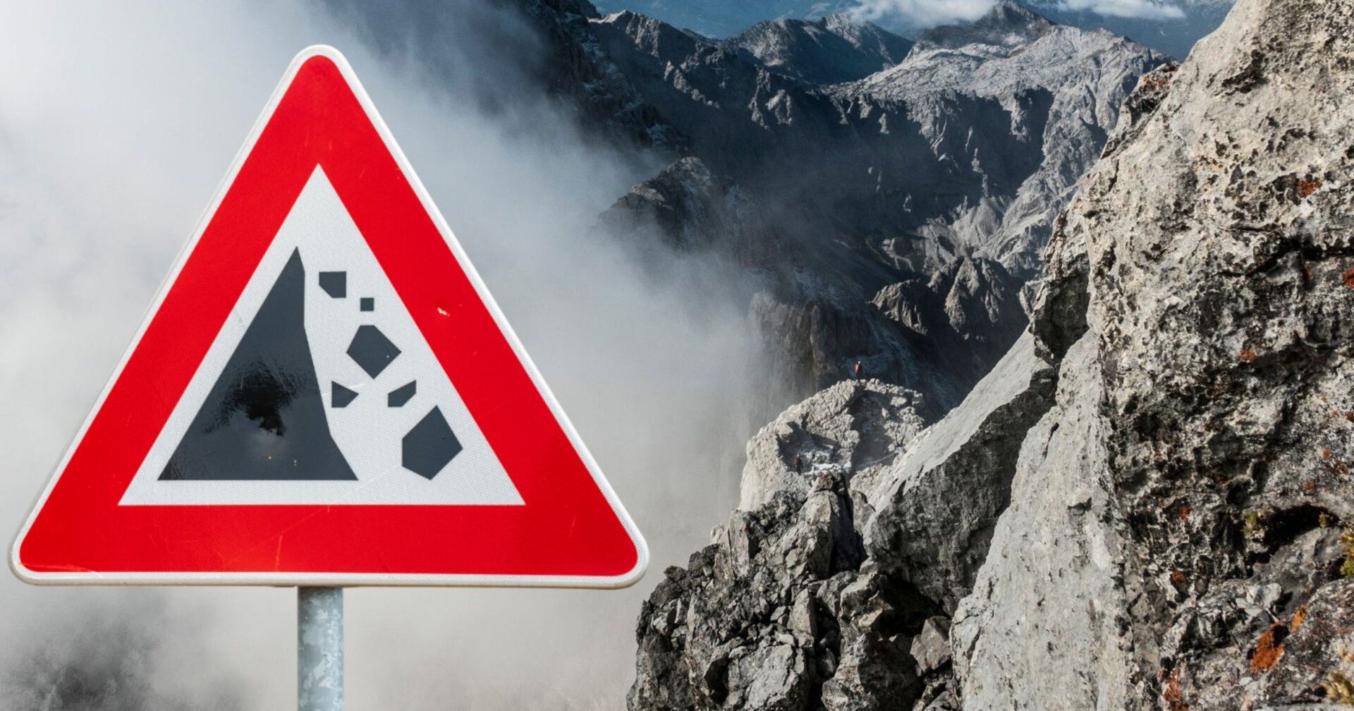 Fotoaufnahme der bayrischen Alpen im nebel, neben einem Warnschild vor Felsstürzen