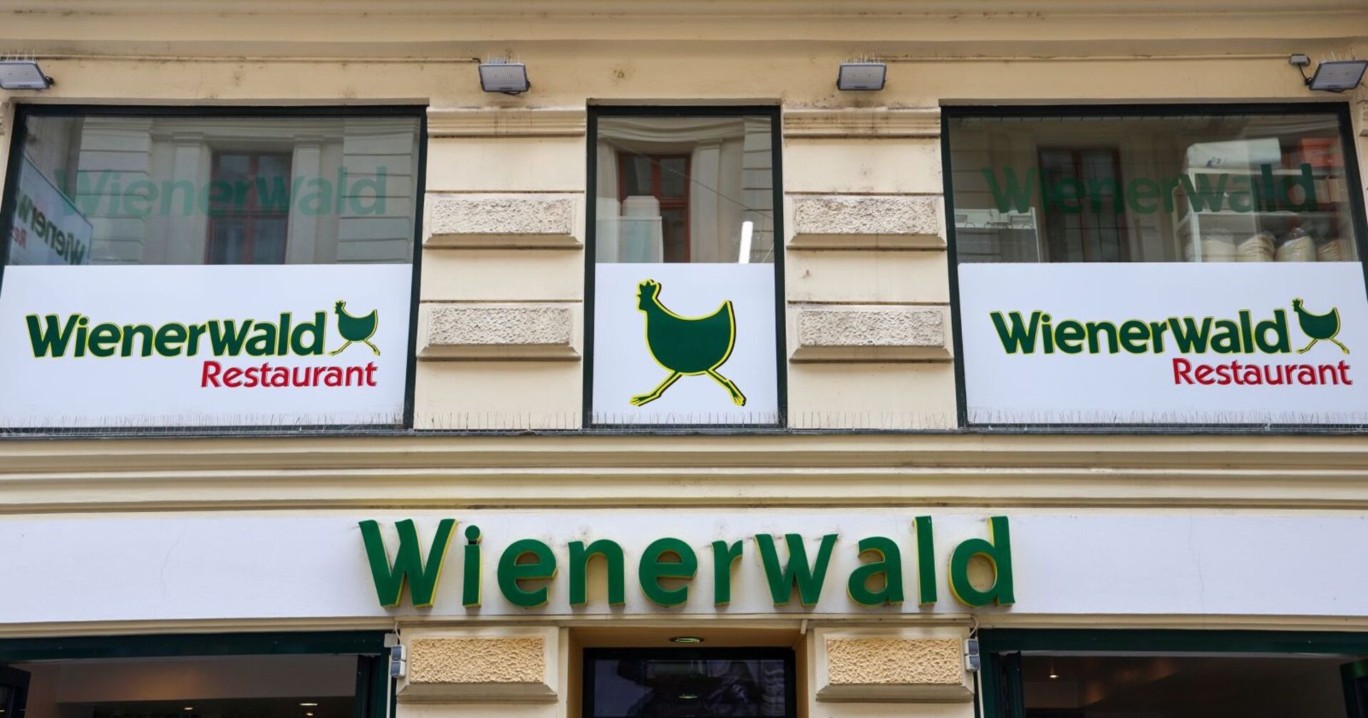 Logo des Wienerwald-Restaurants und Schild mit dem Symbol des laufenden Huhns an einer Gebäudefassade