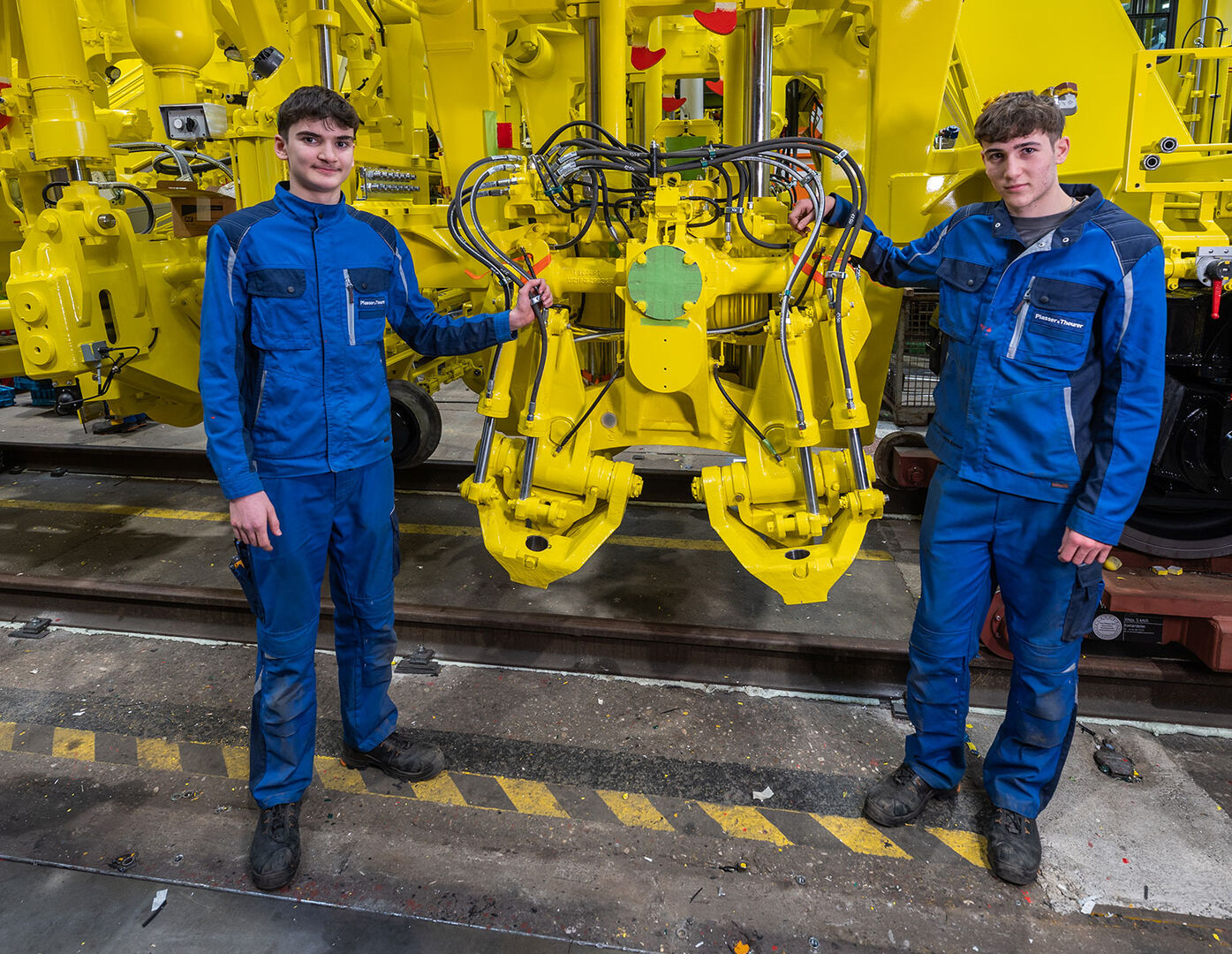 Zwei männliche Lehrlinge in Arbeitskleidung vor einer Maschine | Credit: Plasser &amp; Theurer