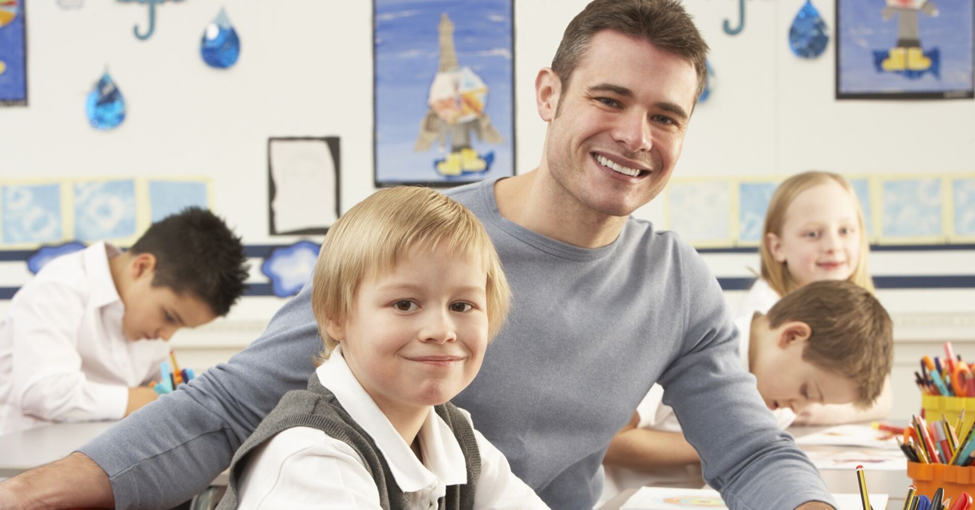 Männlicher Lehrer sitzt neben einem Volkschüler in der Klasse