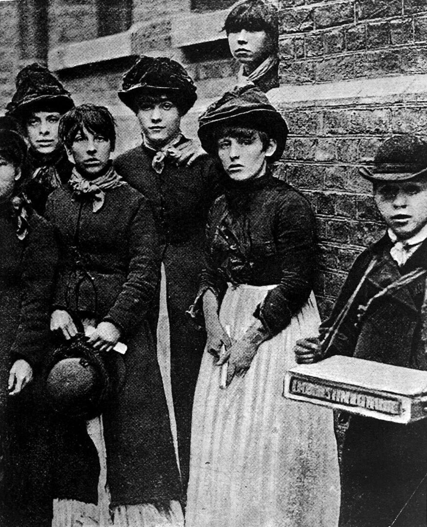 Schwarzweiß-Aufnahme einer Gruppe Jugendlicher, die in einer Streichholzfabrik arbeiten und bereits erste Anzeichen eines „Phossy jaw“ aufweisen