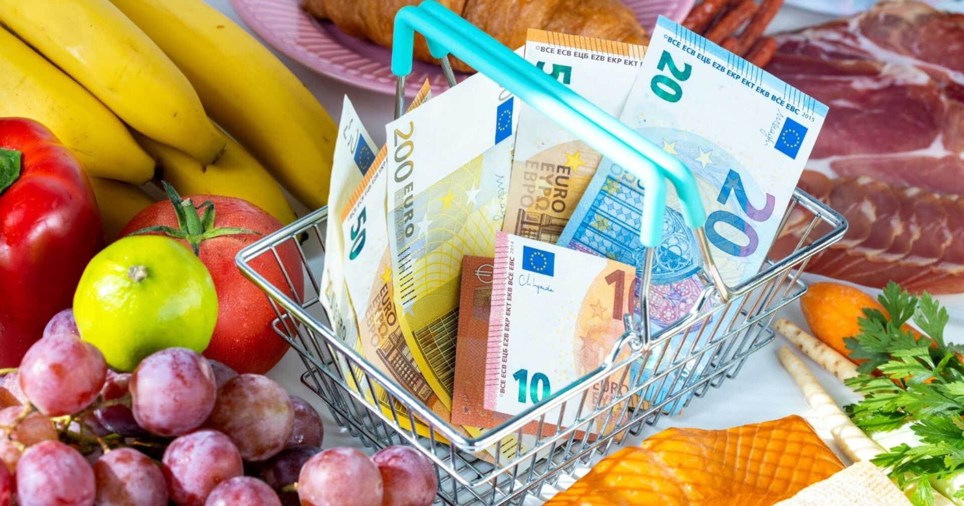 Einkaufskorb mit Euro-Banknoten zwischen Obst, Gemüse, Wurst und Käse – Symbolbild für steigende Lebensmittelpreise.