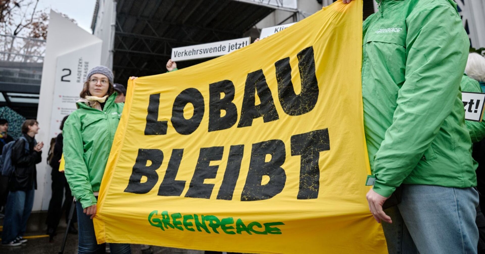 Greenpeace-aktivisten stehen vor dem Infrastrukturministerium und halten ein "Lobau bleibt" Transparent hoch