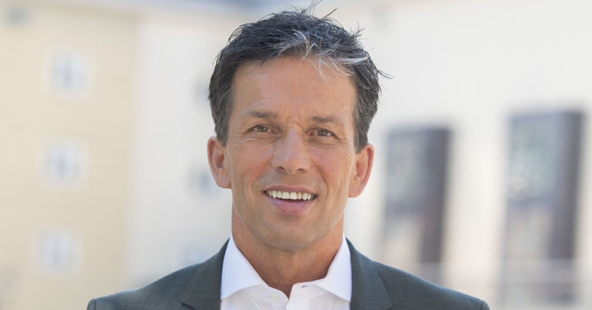 Porträt von Martin Ferdiny im Anzug, er lächelt in die Kamera, Hintergrund unscharf.