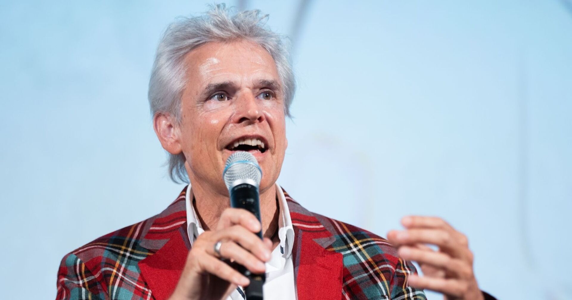 Thomas Brezina spricht mit Mikrofon auf einer Bühne, trägt kariertes Sakko.