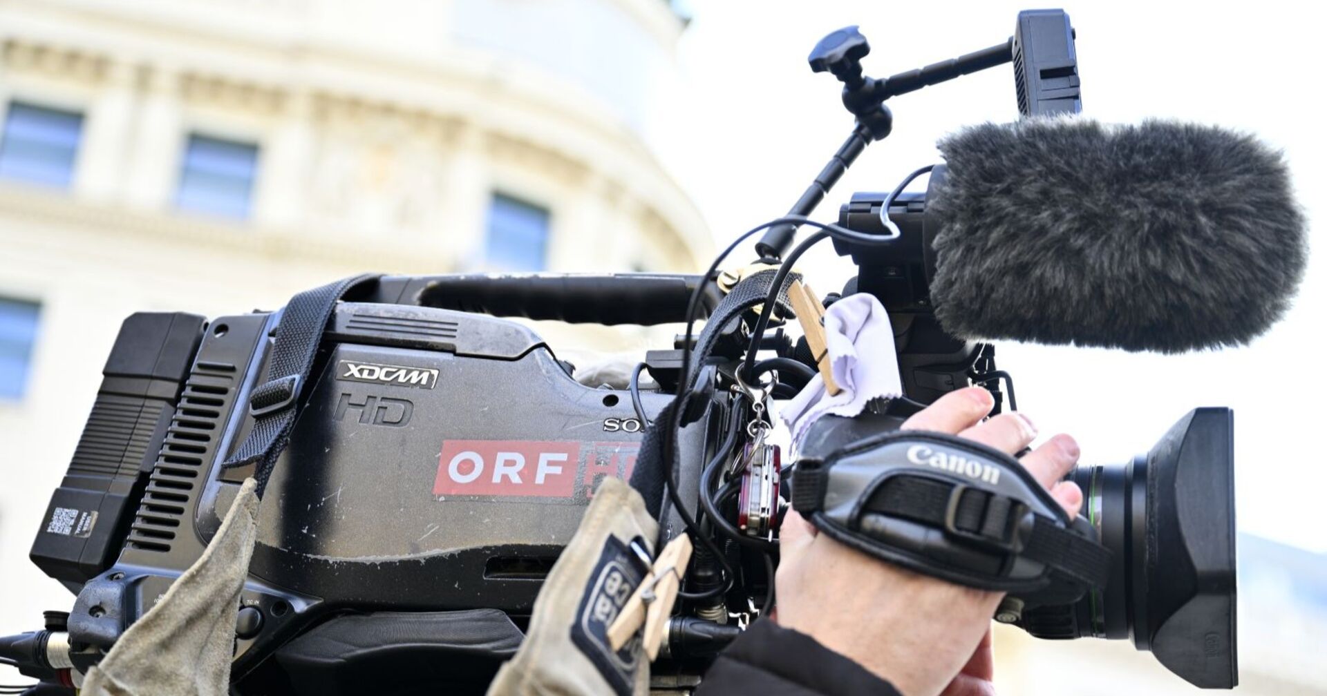 Nahaufnahme einer professionellen ORF-Fernsehkamera mit Mikrofon und Handgriff während eines Außendrehs.
