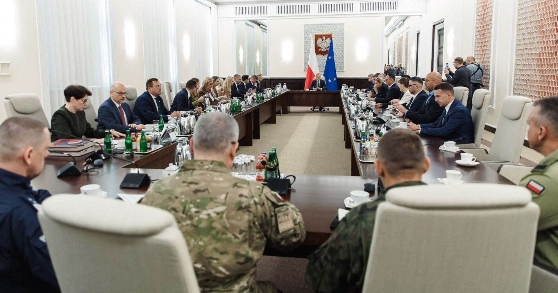 Langer Konferenztisch mit polnischen Regierungsmitgliedern und Militärs in Uniform, Donald Tusk sitzt am Kopfende zwischen polnischer und EU-Flagge.